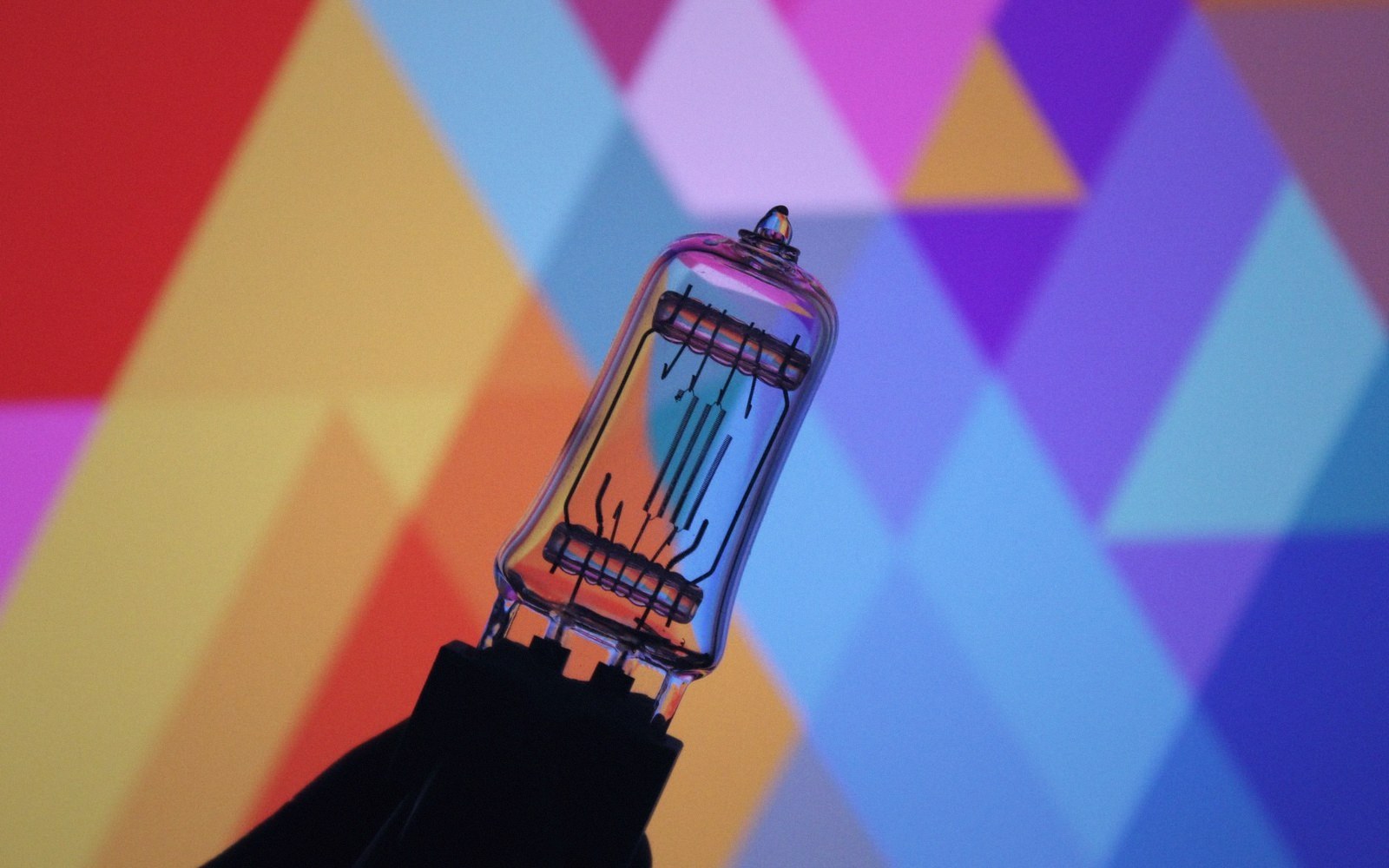 A halogen bulb's glowing filament stands out against a colorful triangle-patterned background