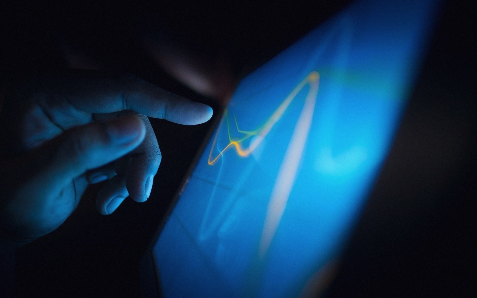 A finger touches a glowing blue touchscreen displaying an illuminated line graph