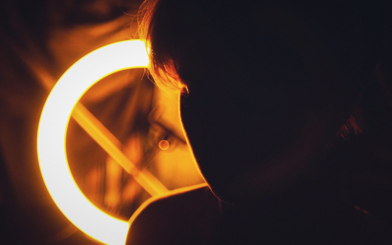 A person's silhouetted head next to a glowing ring light in a dark room