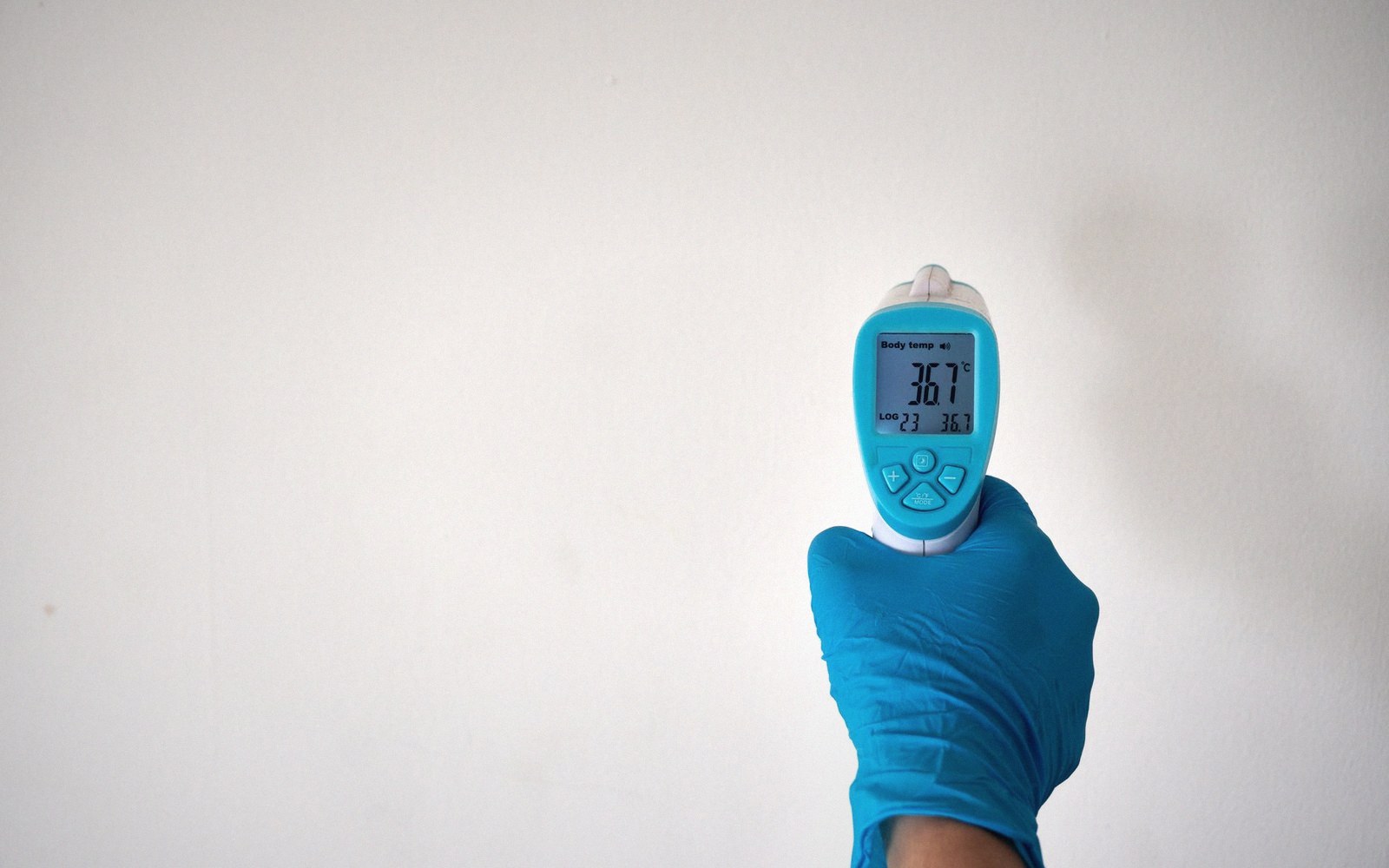 A gloved hand holds an infrared thermometer displaying a body temperature reading of 36.7°C